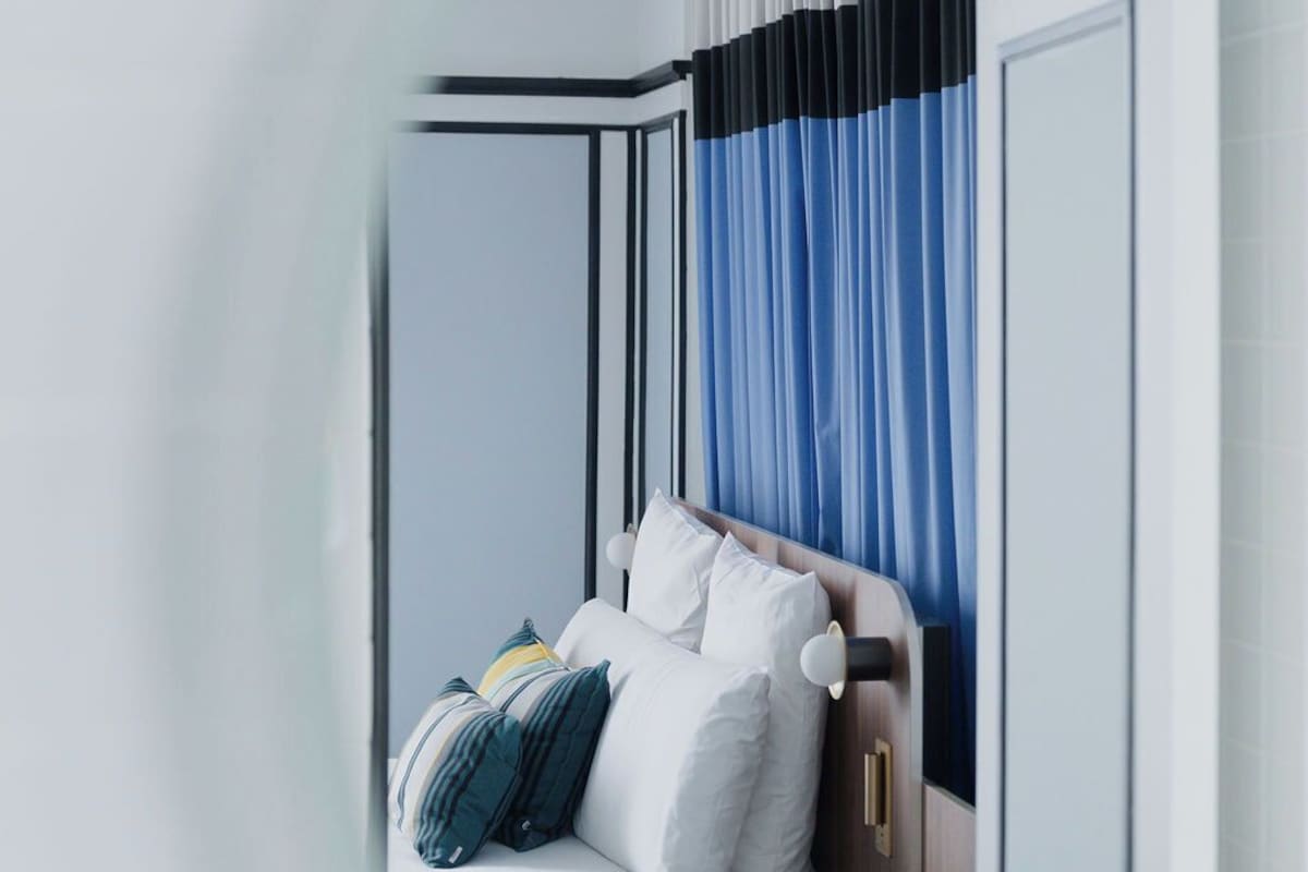 A modern hotel room with a bed, curtains, and a wooden headboard.