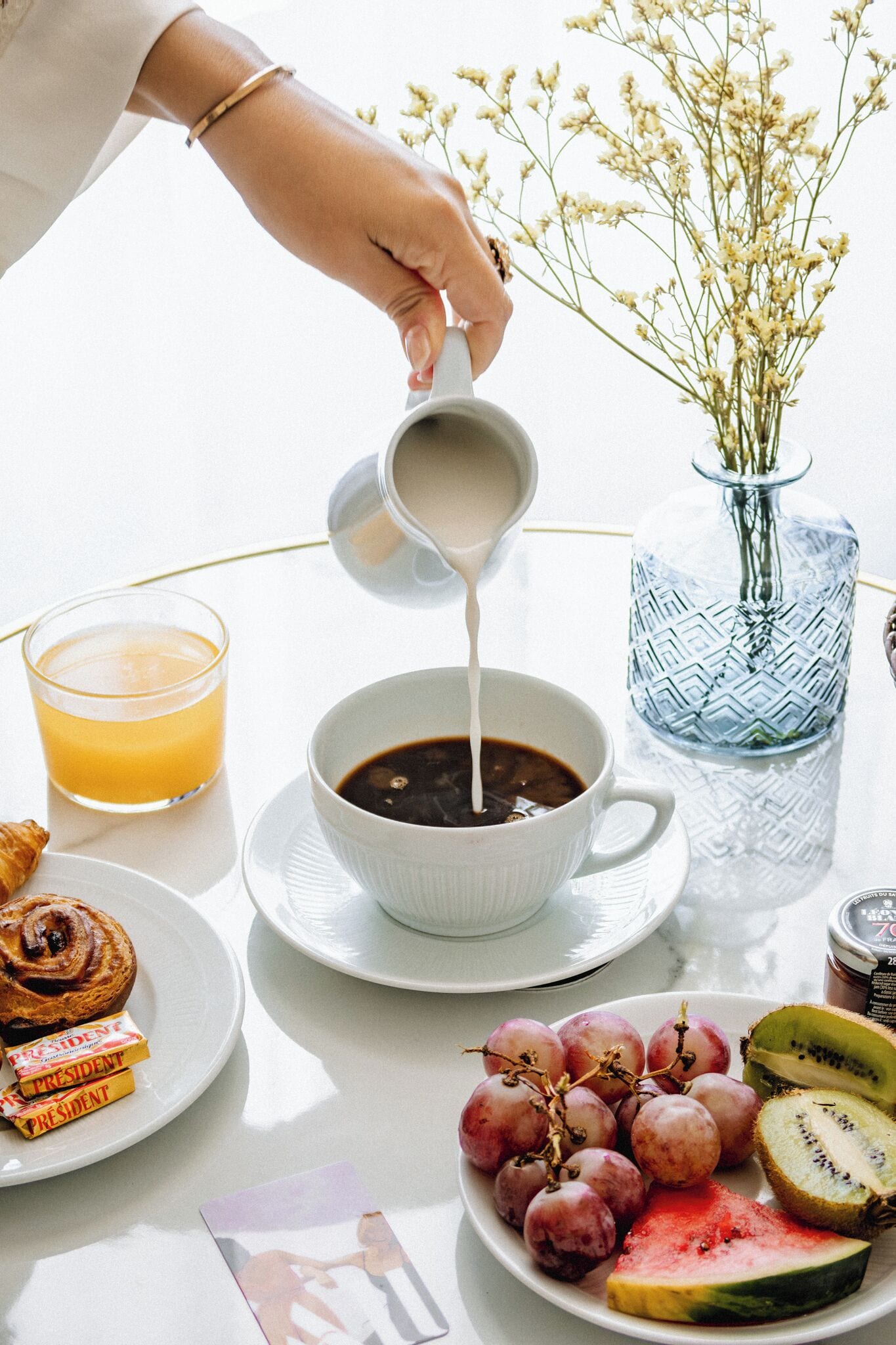 Una escena de desayuno con una taza de café, un vaso de zumo de naranja, un plato con pasteles y un bol de uvas y sandía en rodajas.