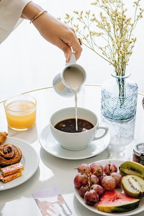 A breakfast setting with a cup of coffee, a glass of orange juice, a plate with pastries, and a bowl of grapes and watermelon slices.