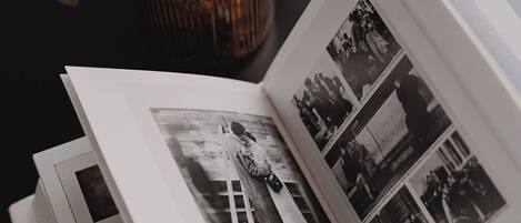 Un libro abierto con fotografías y texto, sobre una superficie oscura, con un jarrón decorativo con flores rosas y hojas verdes al fondo.