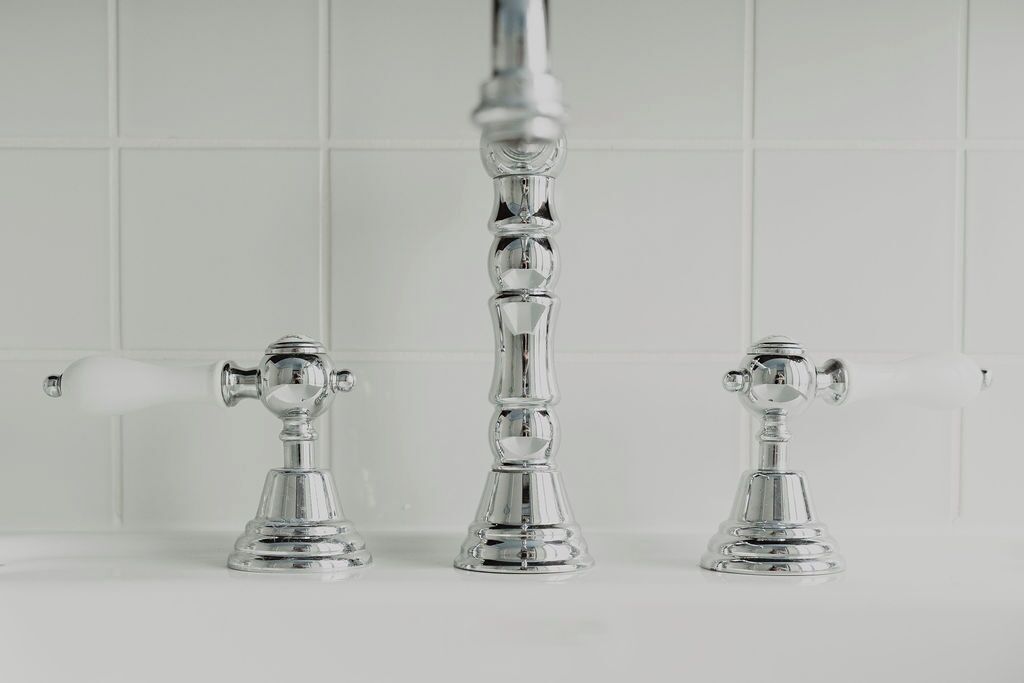 A bathroom with three chrome fixtures, including a faucet and two towel rings, mounted on a white tiled wall.