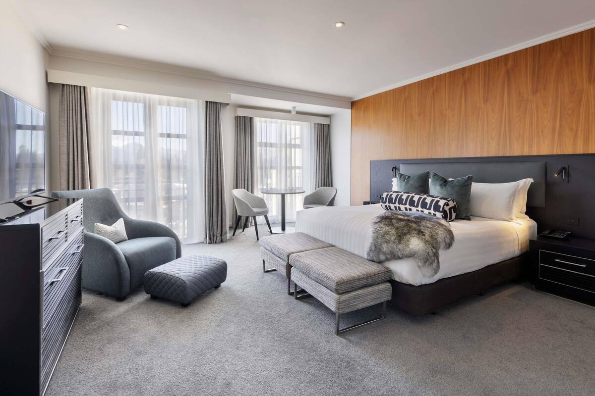 A modern hotel room with a bed, a desk, a chair, and a TV.