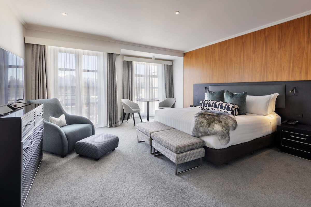 A modern hotel room with a bed, a desk, a chair, and a TV.