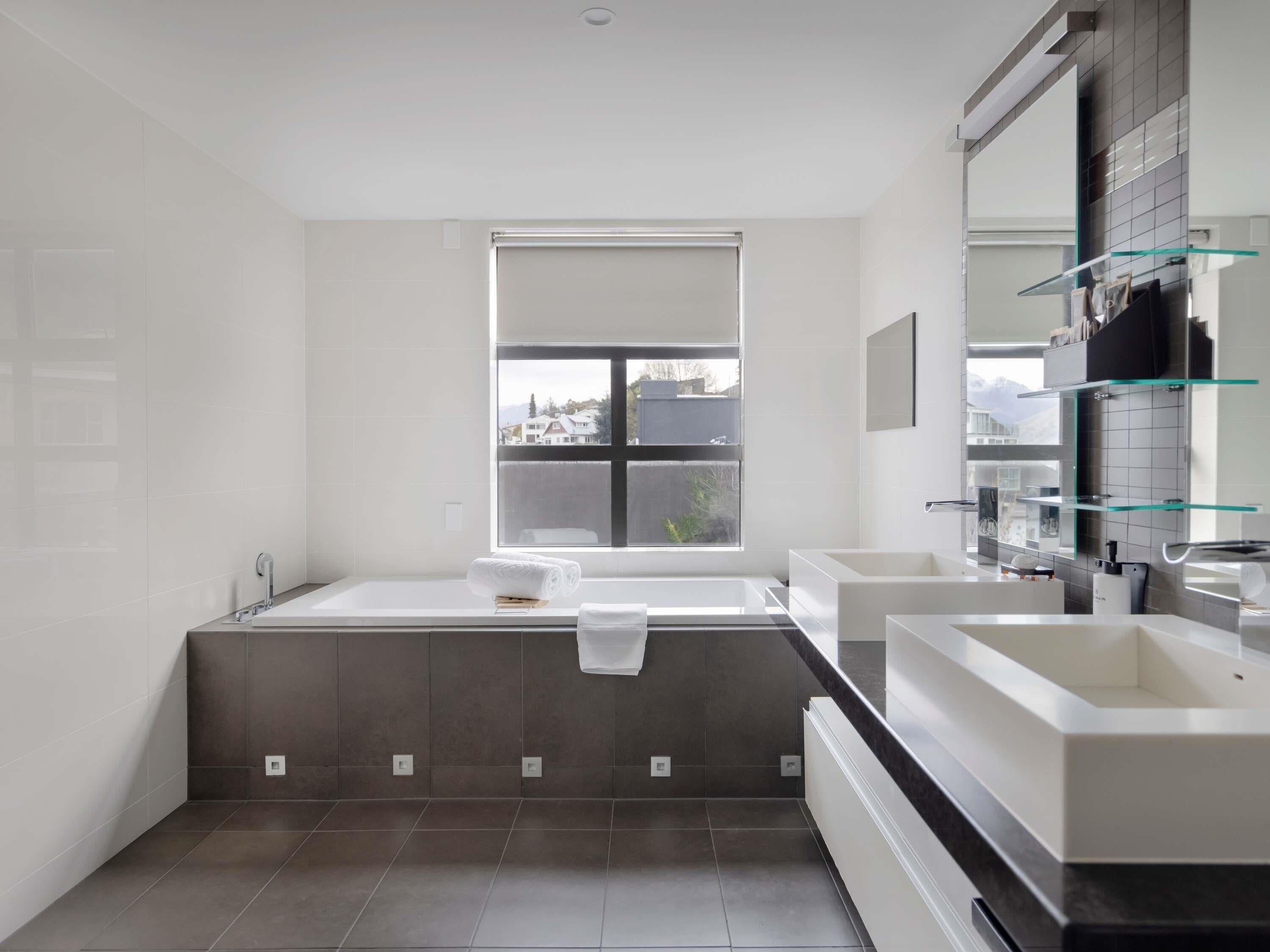A modern bathroom with a large bathtub, two sinks, and a window providing a view.
