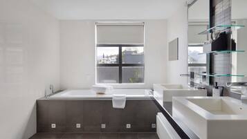 A modern bathroom with a large bathtub, a separate shower area, and a window providing a view of buildings outside.