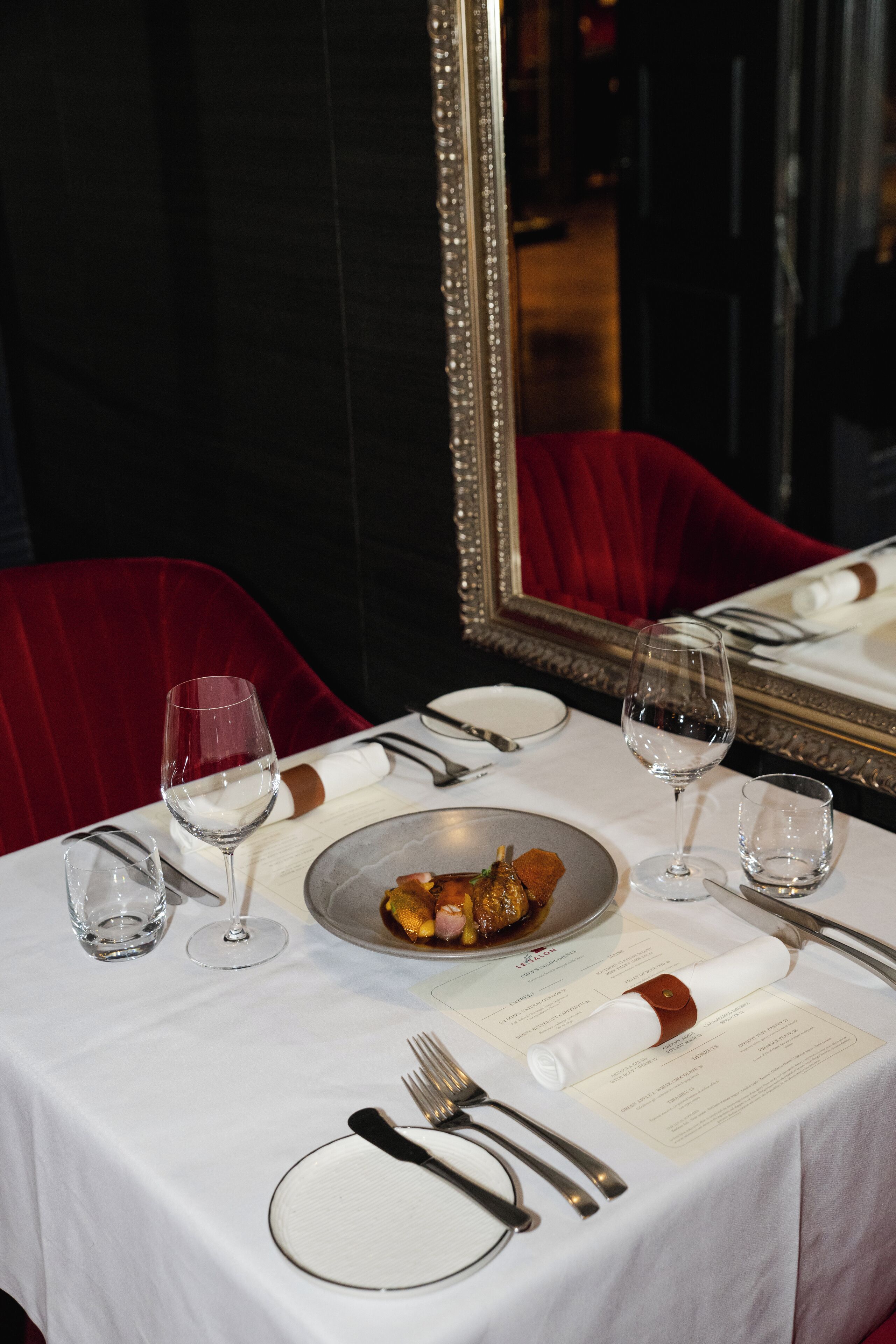 Una mesa de comedor dispuesta con mantel blanco, un plato de comida, copas de vino y cubiertos.