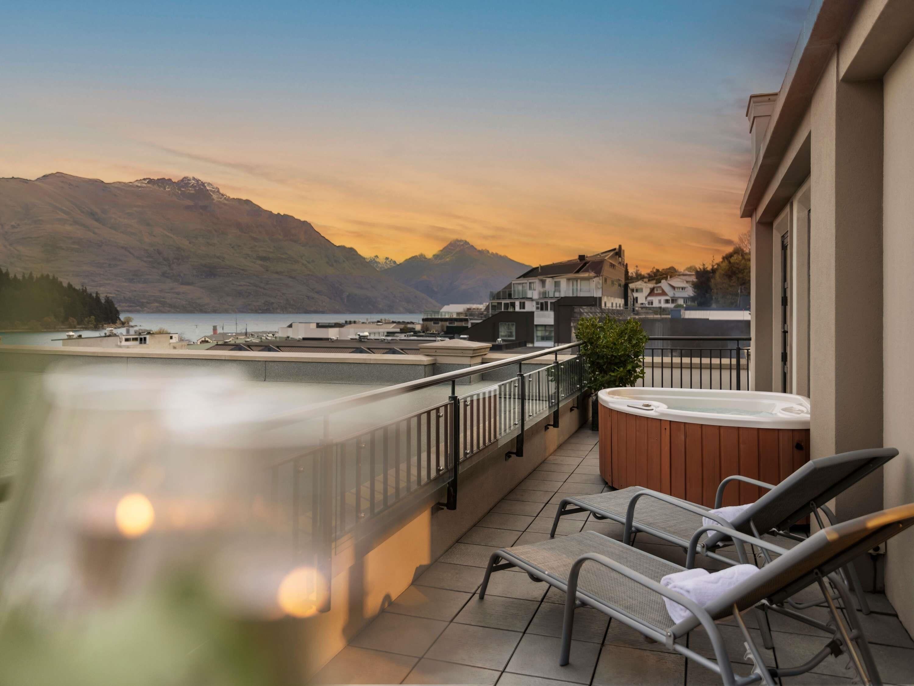 A balcony with a hot tub, lounge chairs, and a view of a lake and mountains.