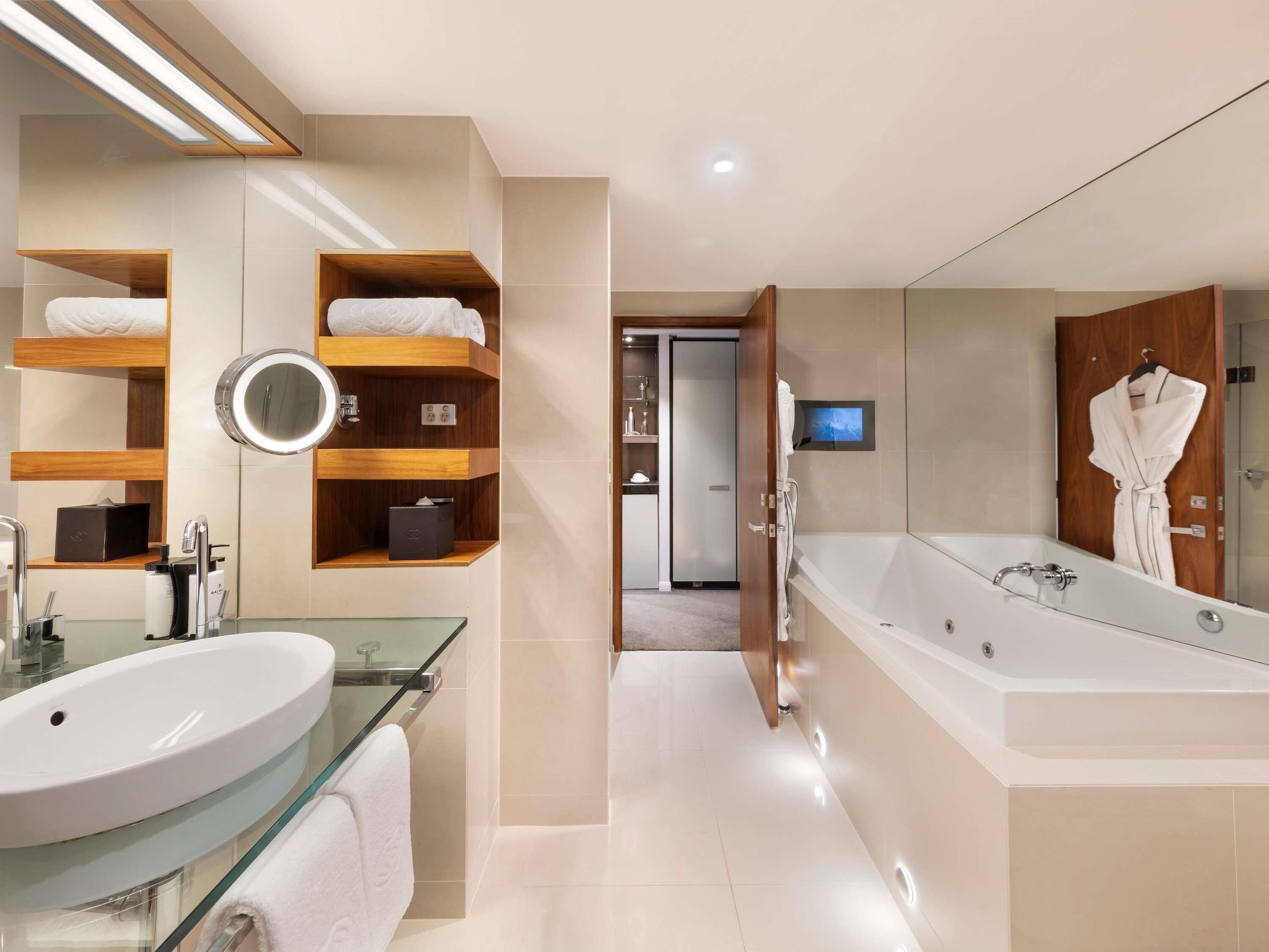 A modern bathroom with a glass-enclosed sink, wooden shelves, a large mirror, and a walk-in shower.