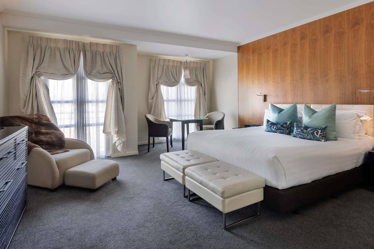 A hotel room with a bed, a seating area with a chair and ottoman, a small table, and a wooden accent wall.