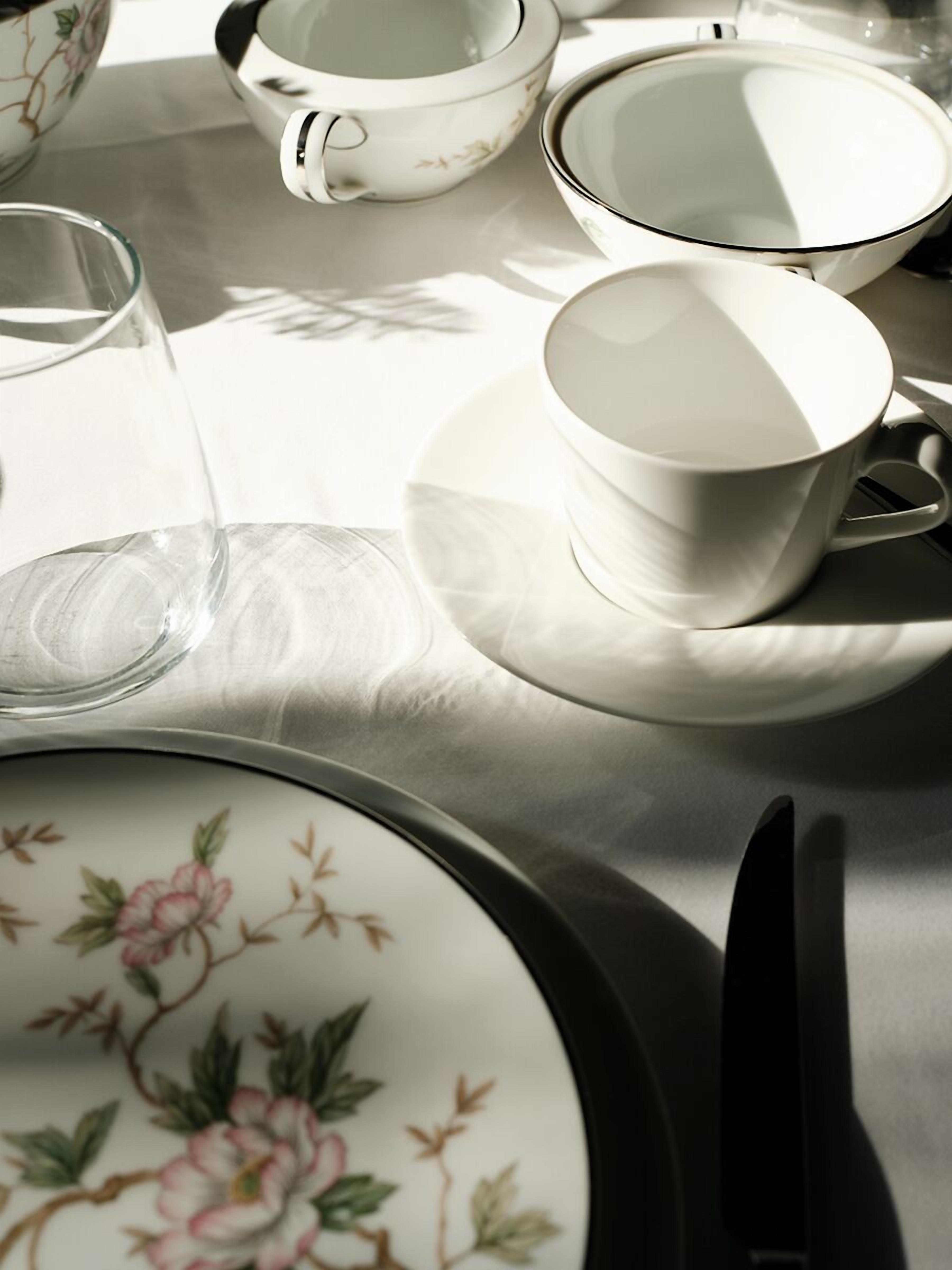 Una mesa dispuesta con vajilla blanca y de estampado floral, que incluye platos, tazas y un vaso.