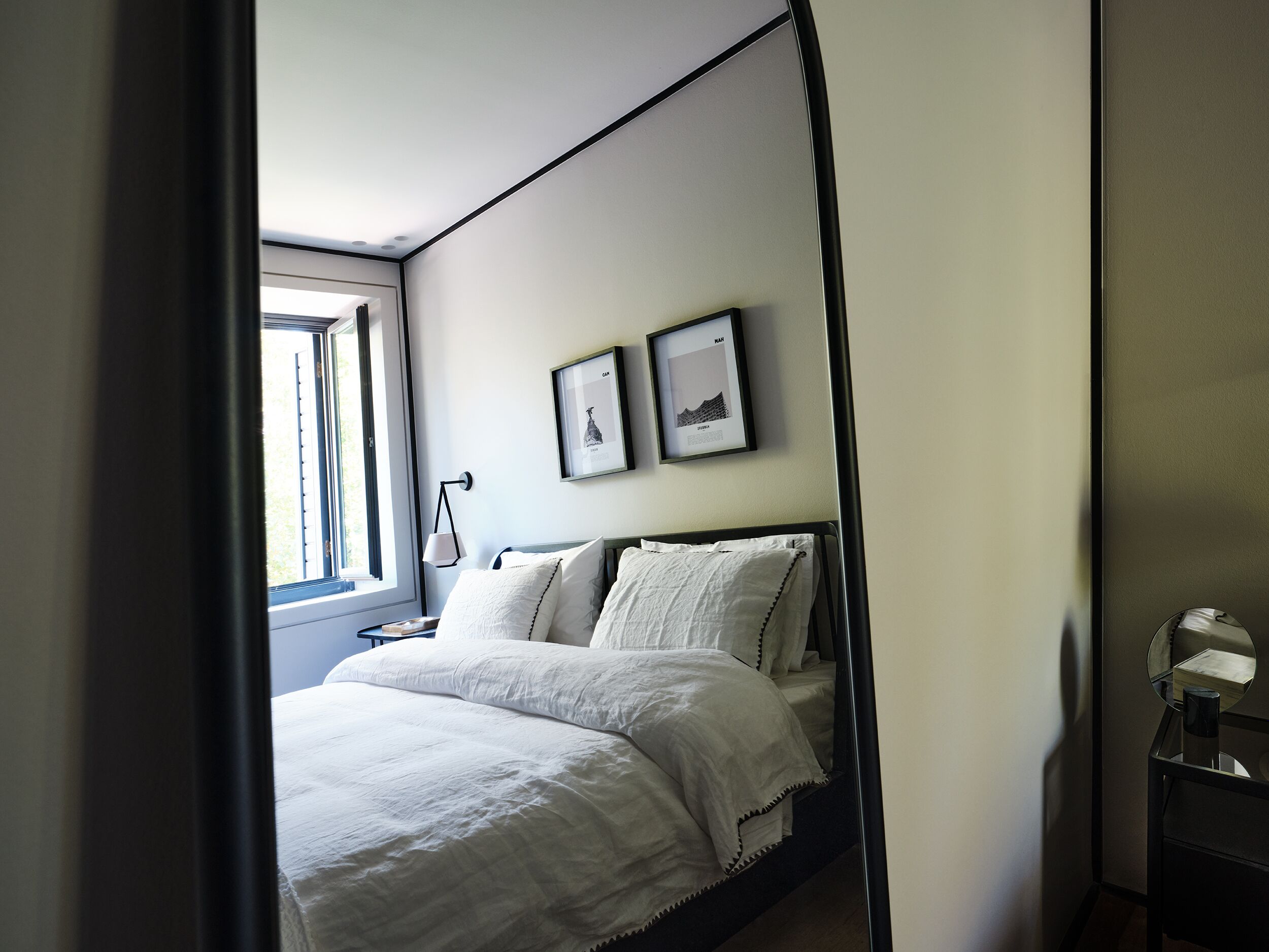 Un dormitorio con cama, mesita de noche, un cuadro enmarco y una ventana.
