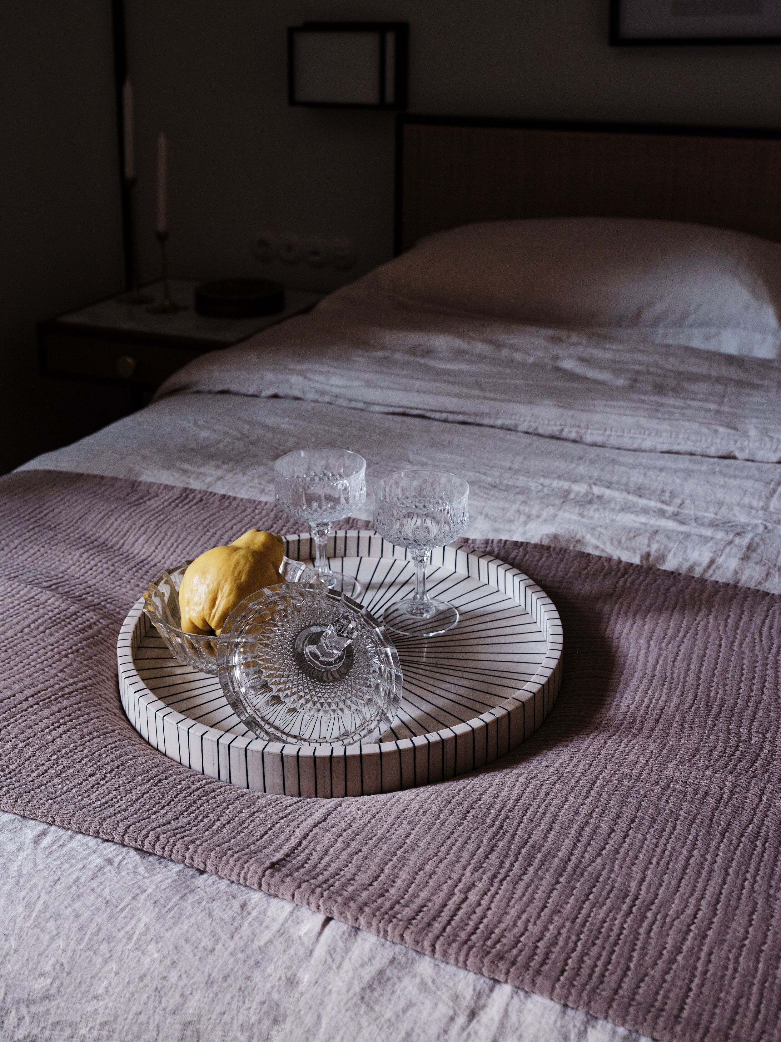 Una cama bien tendida con una colcha blanca y un atril decorativo con un bol y una jarra de vidrio.