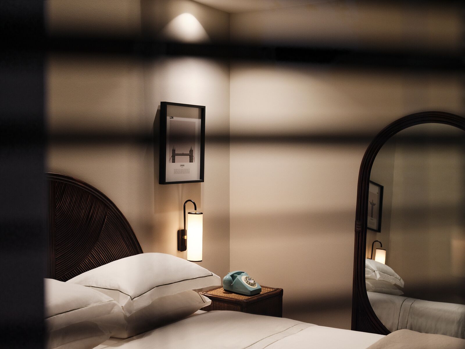 Ein Hotelzimmer mit Bett, Nachttisch mit Lampe, einem London-Bild in einem Rahmen und einem Spiegel.