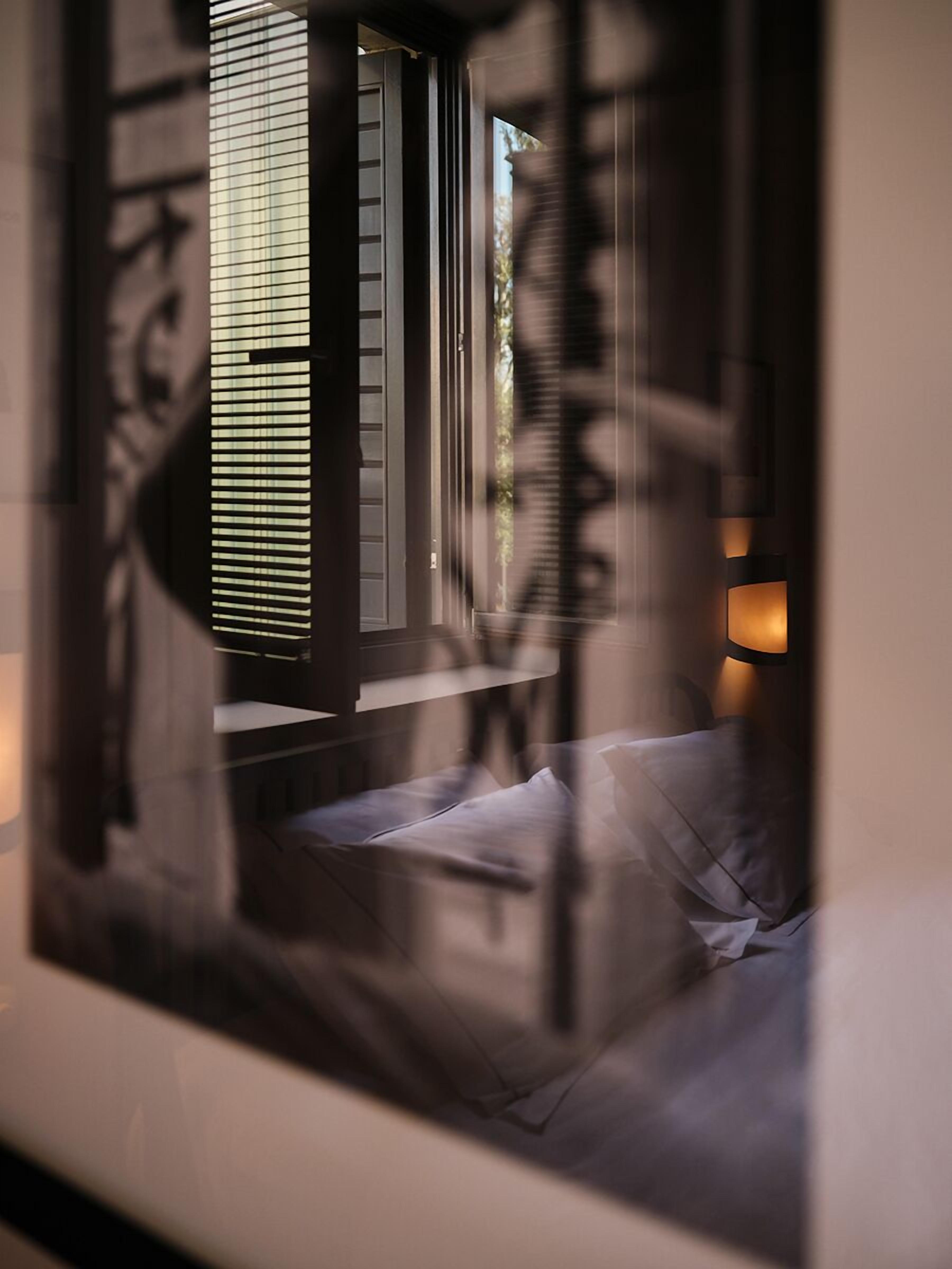 A bedroom with a bed, a window with blinds, and a wall-mounted lamp.