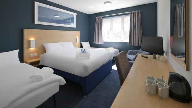 Ein Hotelzimmer mit zwei Betten, einem Schreibtisch, einem Stuhl, einem Fernseher und einem Fenster mit Vorhängen.