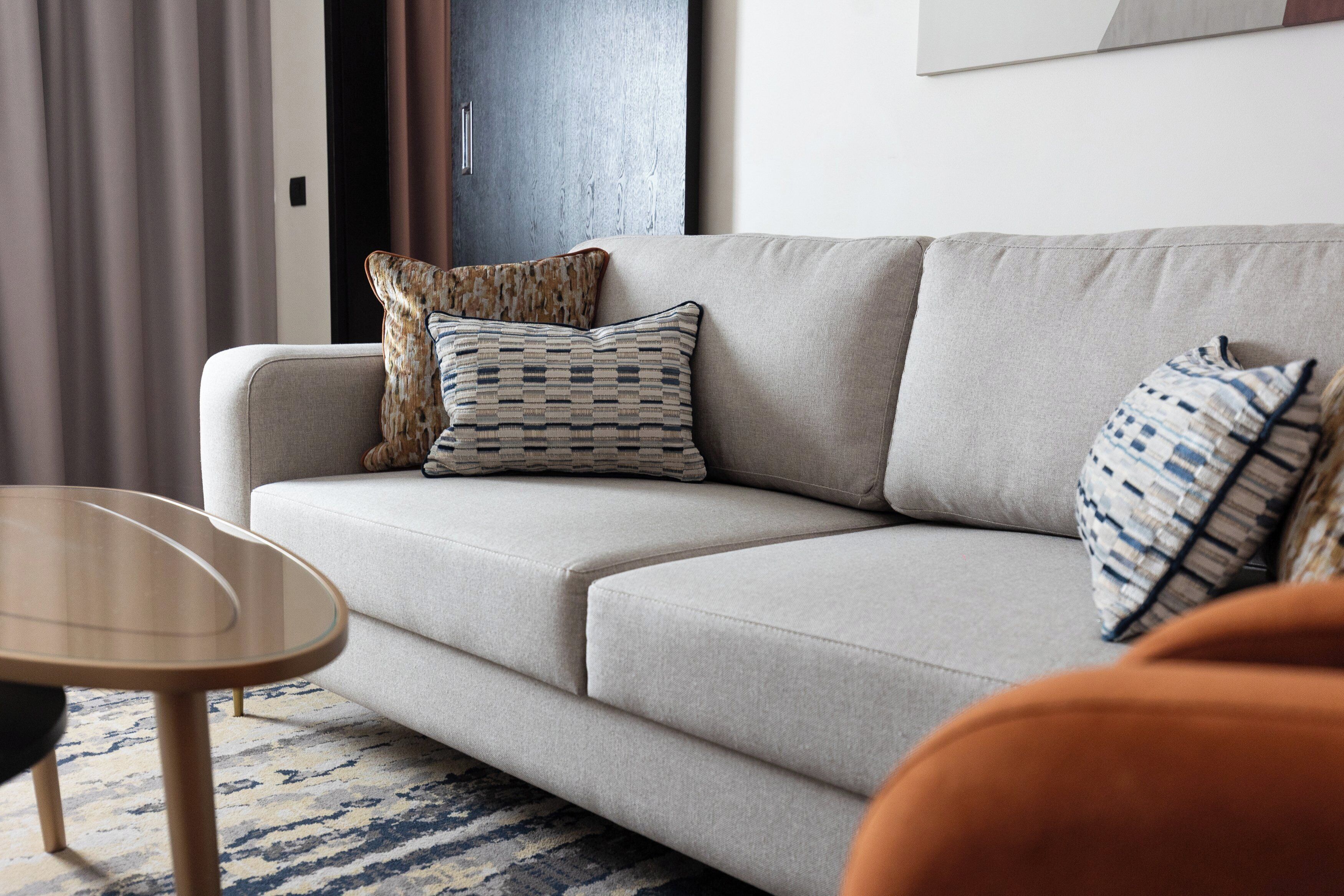 A modern living room with a light grey sofa, patterned cushions, a small wooden coffee table, and a blue and white patterned rug.