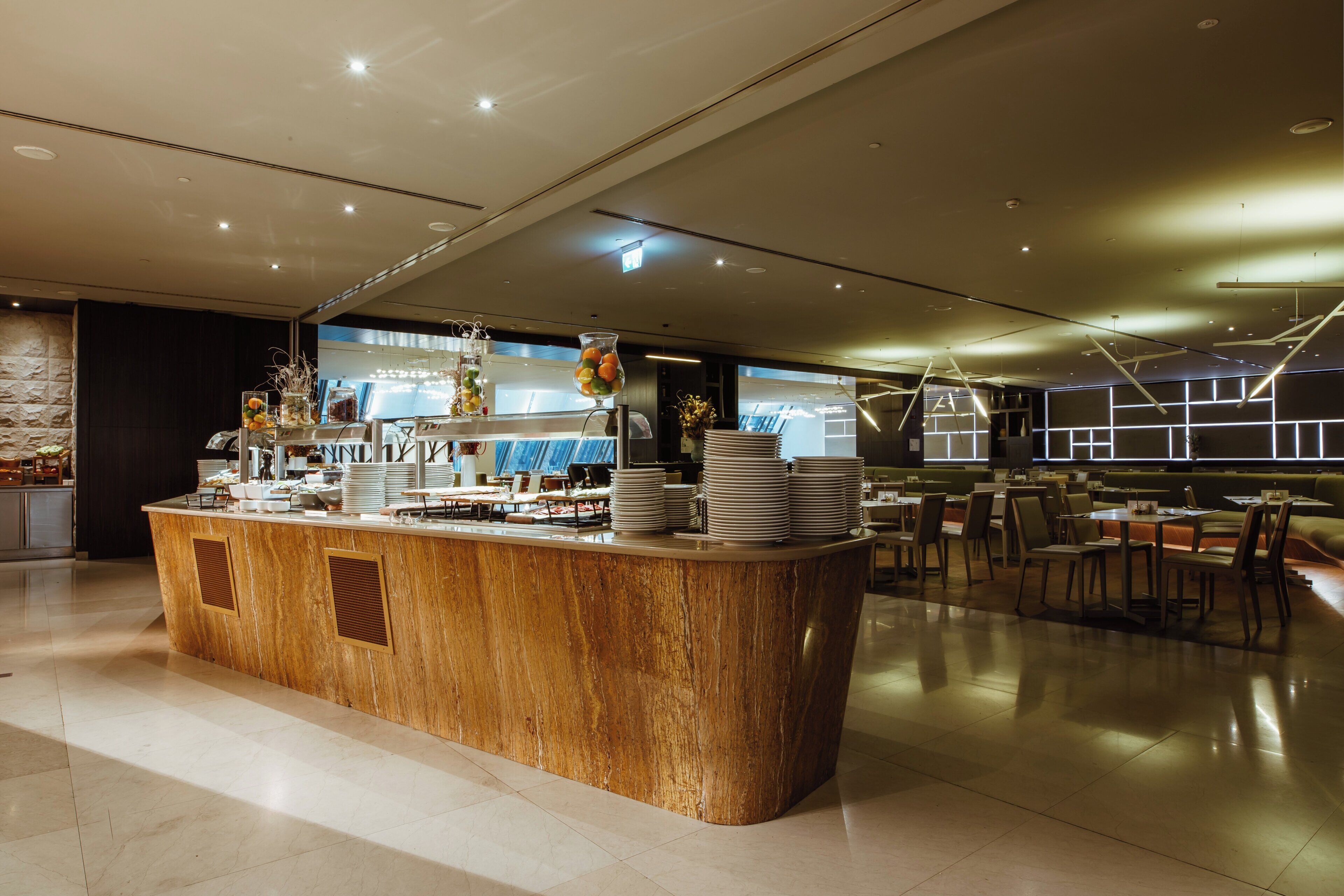 A modern restaurant with a central wooden counter, multiple dining tables, and a contemporary interior design.