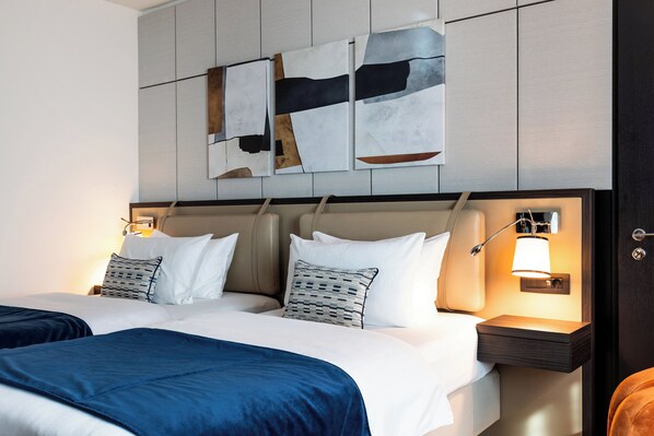 Une chambre d’hôtel moderne avec un grand lit, deux tables de chevet et des œuvres d’art abstraites accrochées au mur.