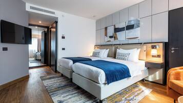 Ein modernes Hotelzimmer mit zwei Betten, einem Flachbildfernseher, einem Nachttisch mit Lampe und einem großen abstrakten Kunstwerk über dem Bett.