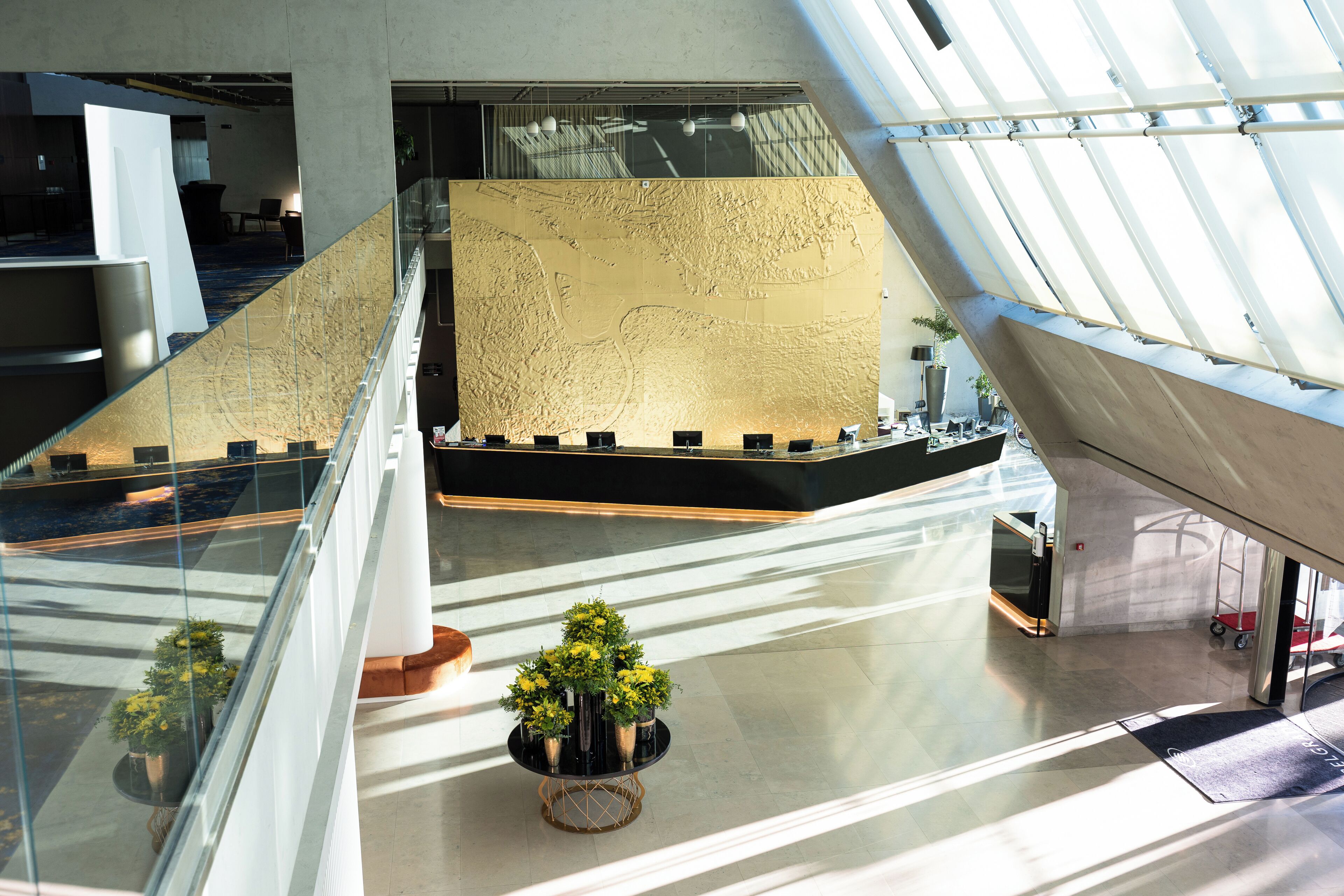 A modern interior with a glass railing, a central seating area with plants, and a large textured wall.