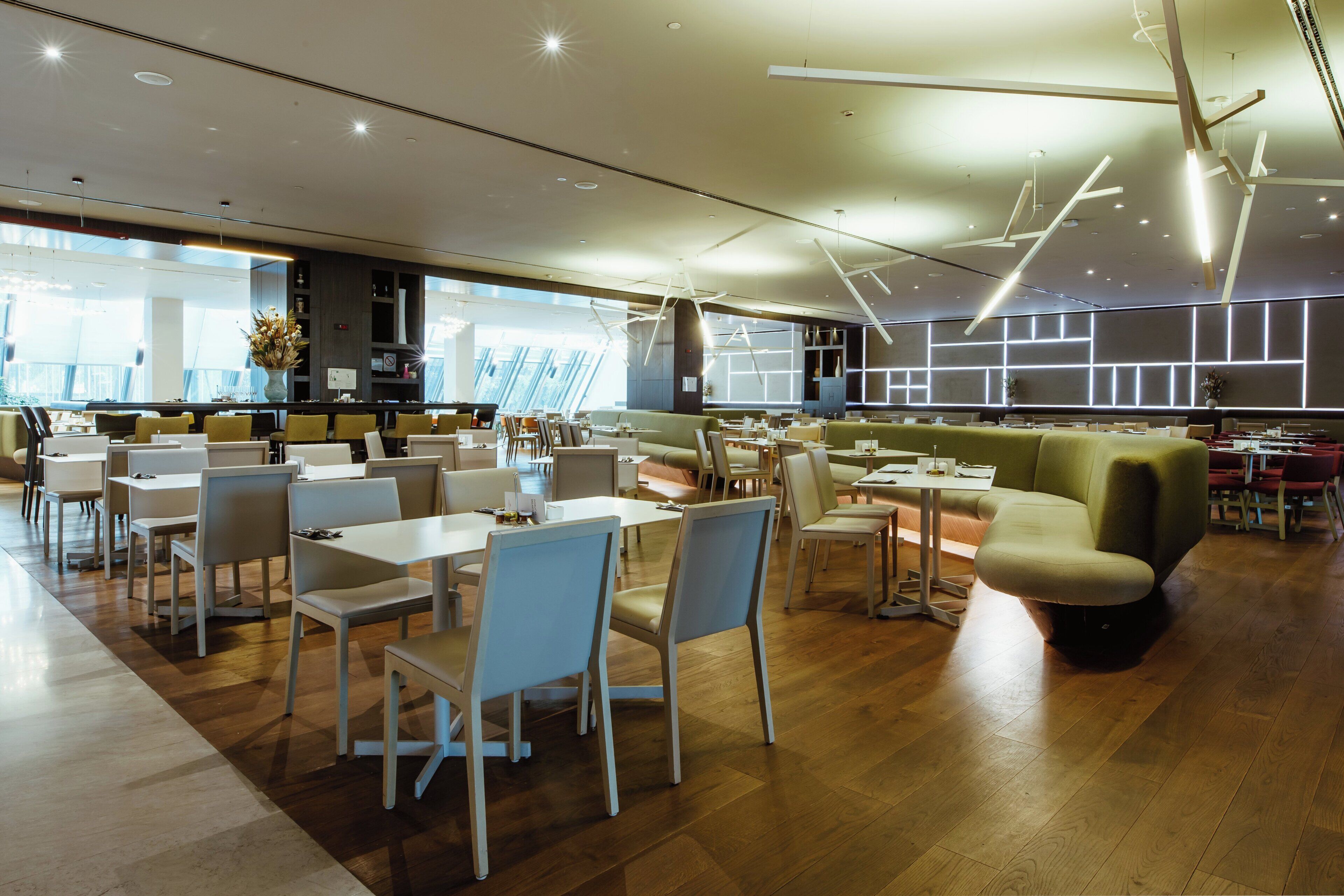 A modern restaurant with white tables and chairs, a green sofa, and a wooden floor.