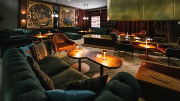 A modern lounge area with sofas, armchairs, and tables, featuring ambient lighting and a large mural on the wall.