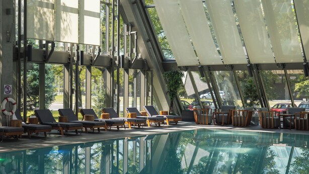 An indoor swimming pool with lounge chairs and sunshades, surrounded by large windows. - Crowne Plaza Belgrade by IHG (Belgrade)