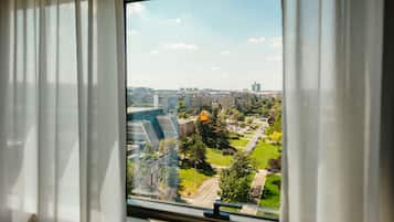 Une vue à travers une fenêtre ornée de rideaux blancs, dévoilant un paysage urbain avec des bâtiments, un pont et des espaces verts.