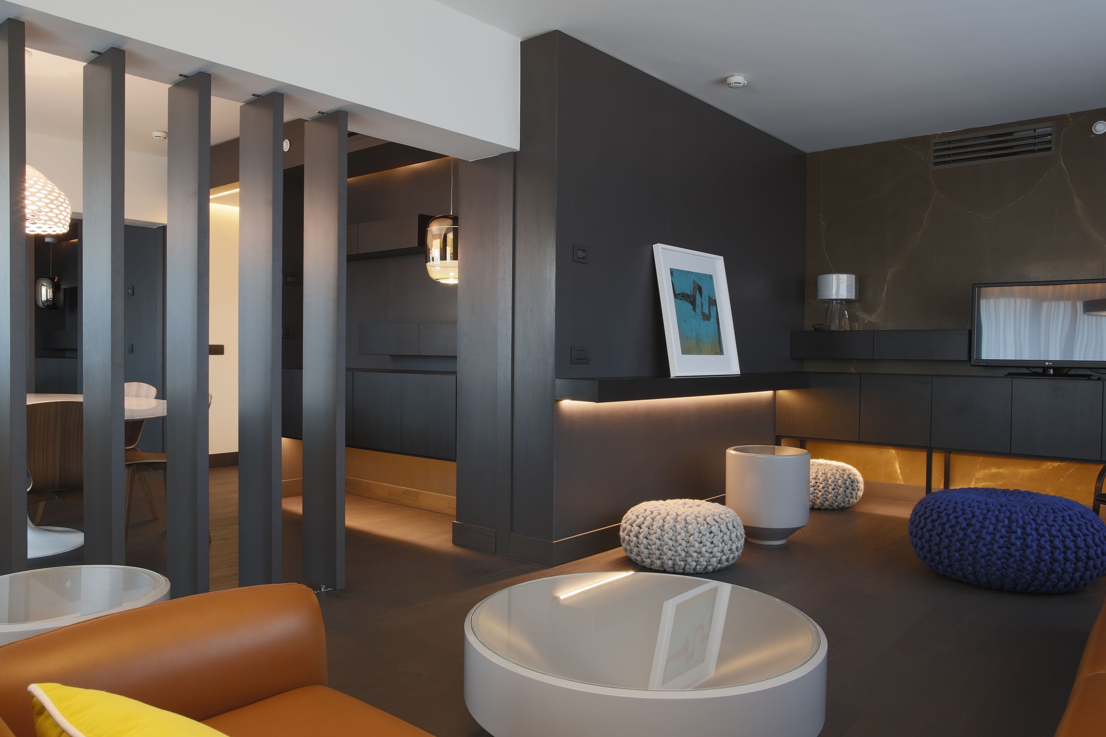 A modern living room with a sofa, ottomans, a round coffee table, and a TV.