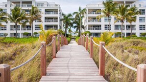 A wooden boardwalk leading to a modern hotel with balconies and palm trees. - Le Vele Resort (Providenciales)