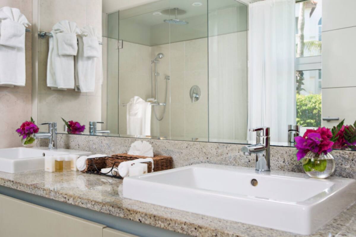 Ein Badezimmer mit zwei Waschbecken, einer Dusche und einem großen Spiegel. Handtücher hängen an einem Wäscheständer und auf der Ablagefläche steht ein Korb mit Toilettenartikeln.