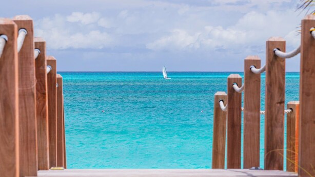 A wooden deck leading to turquoise waters with a sailboat in the distance. - Le Vele Resort (Providenciales)