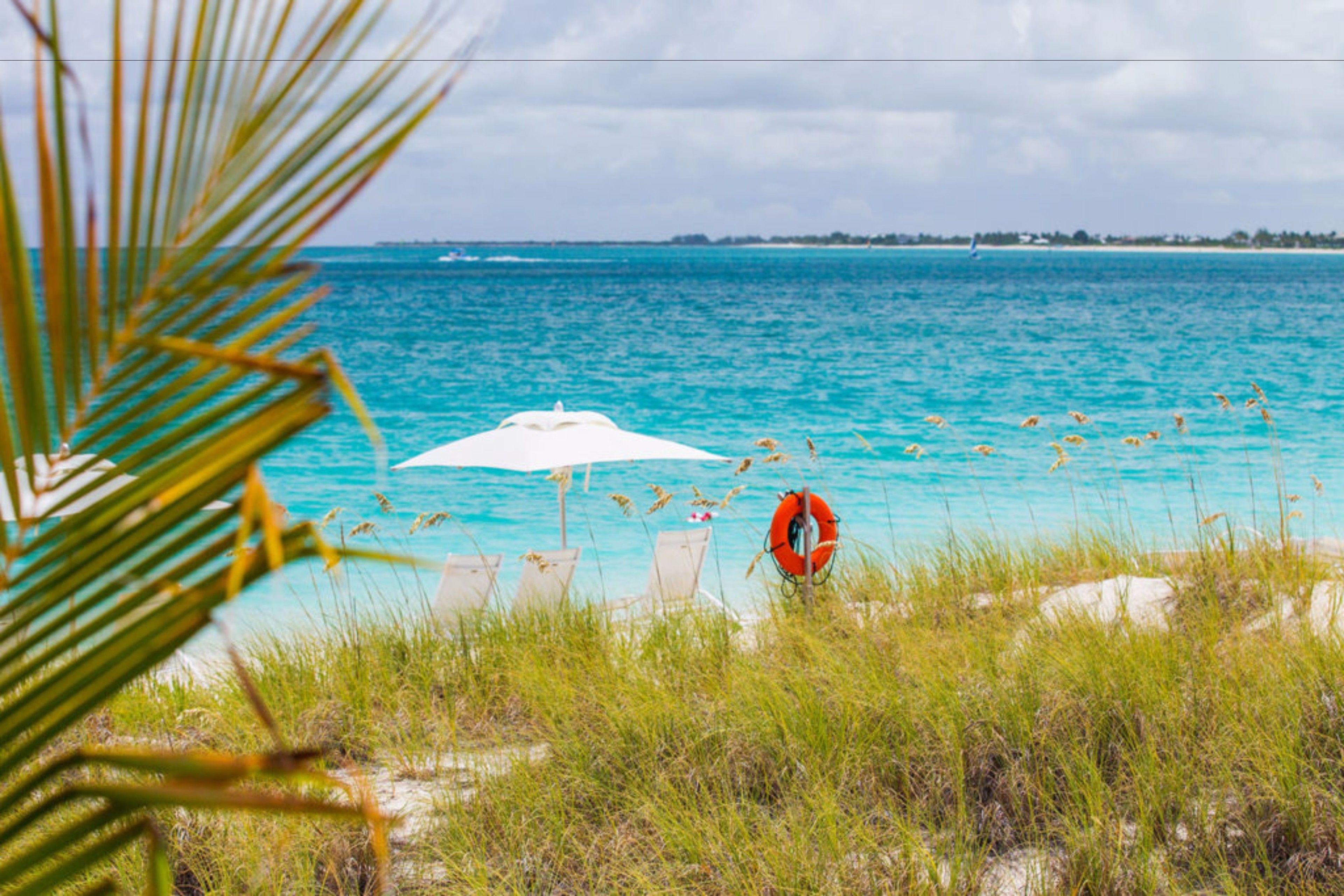 A beach with a white umbrella and a lifebuoy, clear turquoise water, and distant shoreline.
