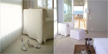 Una habitación con una cama cubierta de sábanas blancas, una mesita pequeña con una lámpara y vistas al mar desde un balcón.