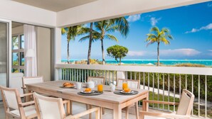 A wooden table with breakfast items, a view of the ocean with palm trees, and a balcony railing. - Le Vele Resort (Providenciales)