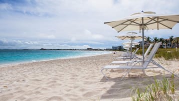 A beach with white lounge chairs and umbrellas, a sandy shore, and a calm sea.