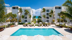 A resort with a central pool, lounge chairs, and palm trees. - Le Vele Resort (Providenciales)