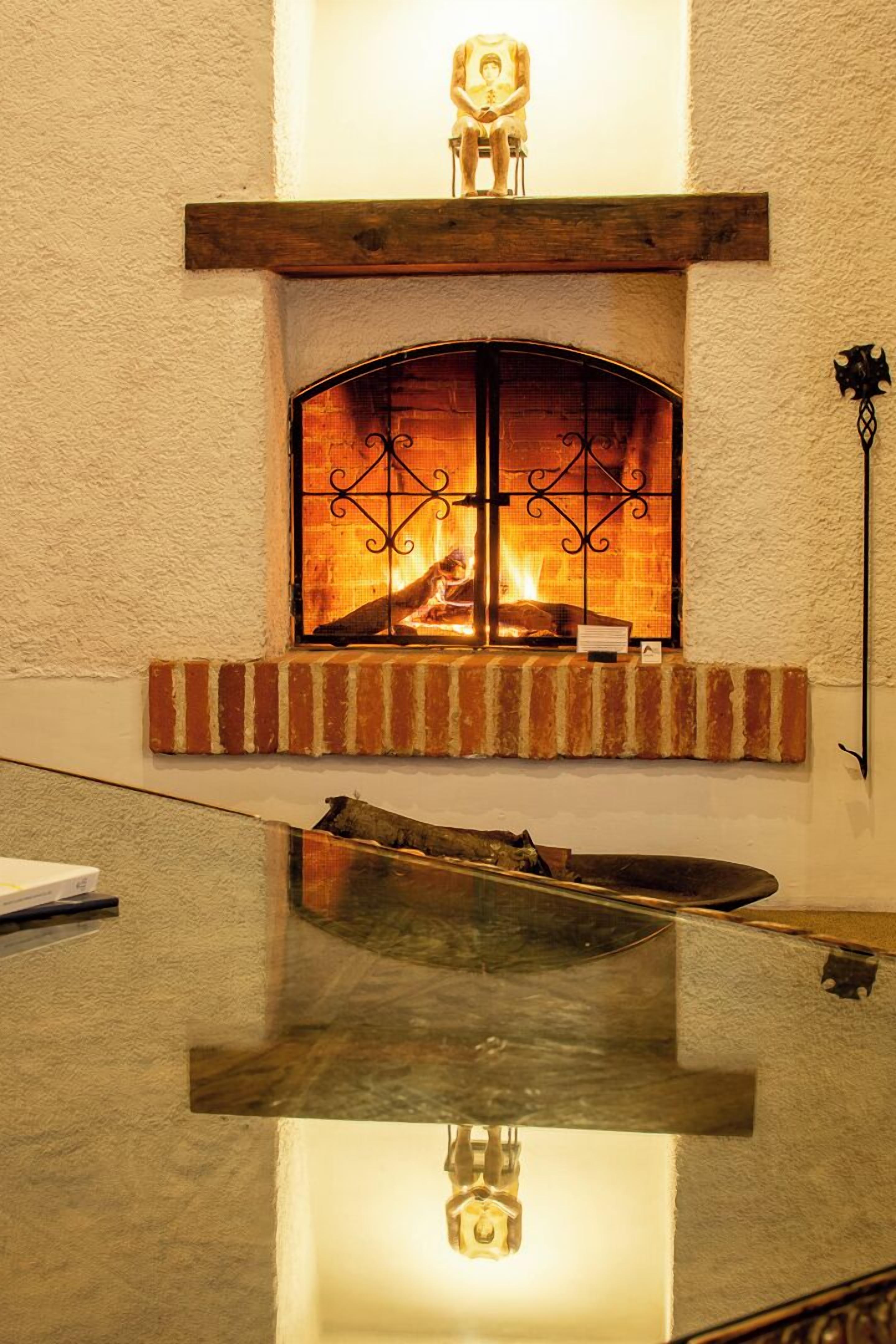 Una chimenea con repisa de piedra, un banco de madera y un gato sentado en él.