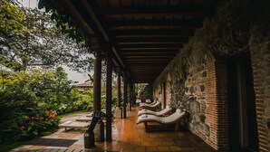 A covered outdoor area with lounge chairs and a stone wall. - Hotel Museo Spa Casa Santo Domingo (Antigua Guatemala)