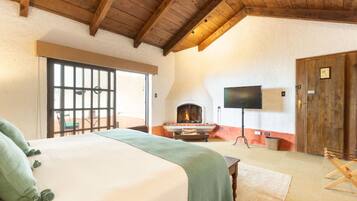A bedroom with a large bed, a fireplace, a television, and a wooden ceiling.