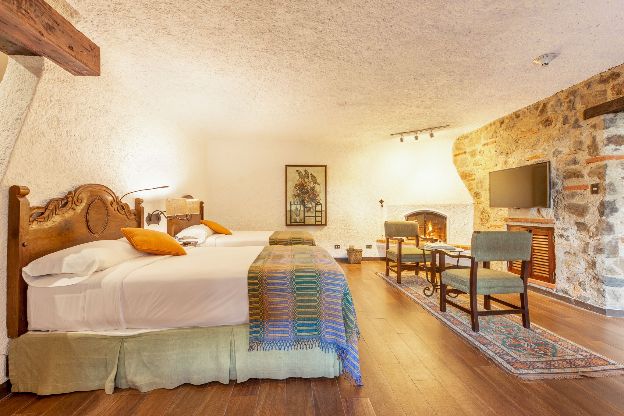 A bedroom with a large bed, a television, a fireplace, and a stone wall.