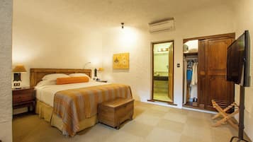 A bedroom with a bed, bedside table, lamp, and a wooden chest. There is a wardrobe and a television.