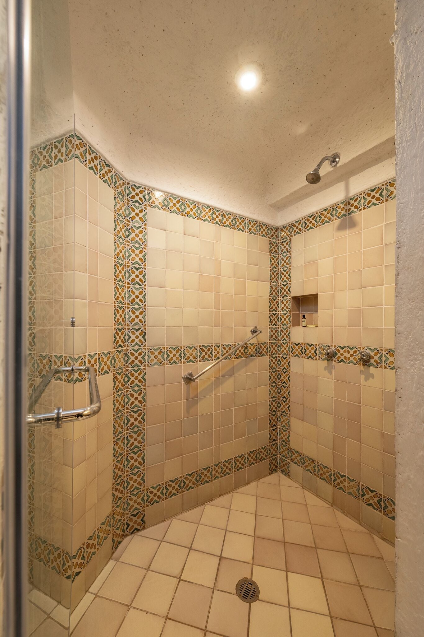 Une douche à l’italienne avec des carreaux décoratifs, une barre d’appui et un pommeau de douche.