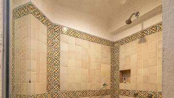 A walk-in shower with patterned tiles, a handrail, and a showerhead.