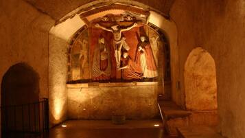 A dimly lit interior with a fresco depicting a religious scene on the wall.