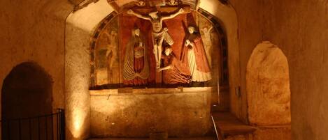 Un interior tenuemente iluminado con un fresco que representa una escena religiosa en la pared.