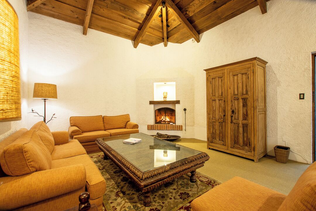 A cozy living room with a fireplace, wooden furniture, and a high ceiling.