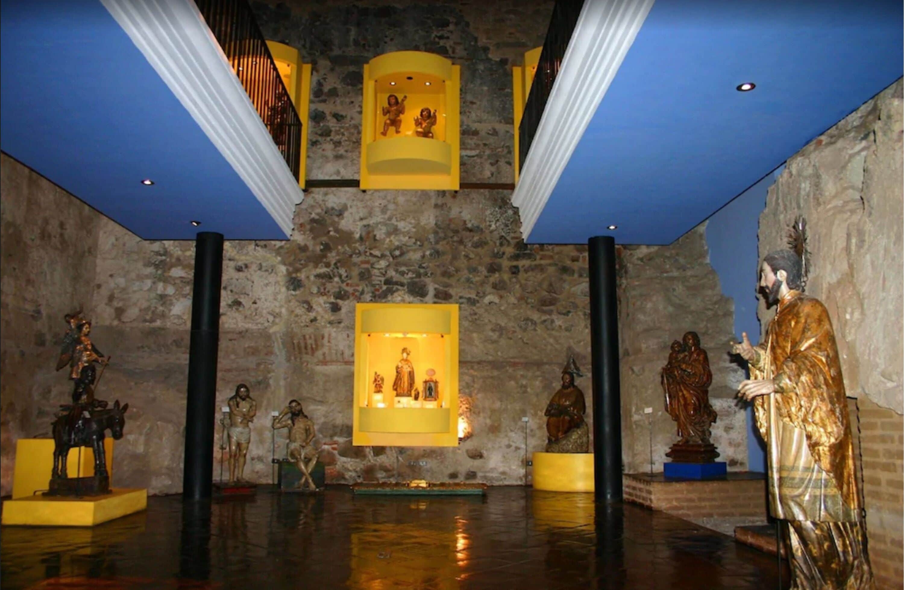 A museum interior with stone walls, yellow display cases, and various statues.
