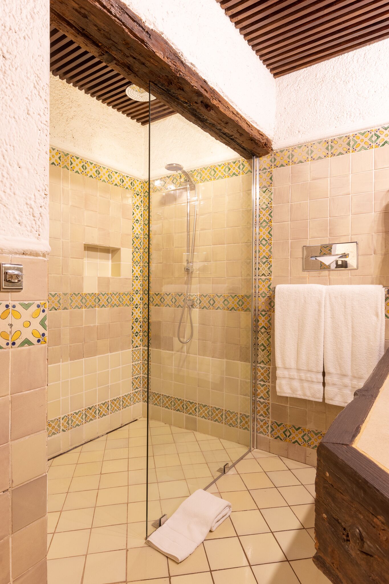 Een douche met een glazen deur, betegelde wanden en een houten plafond.