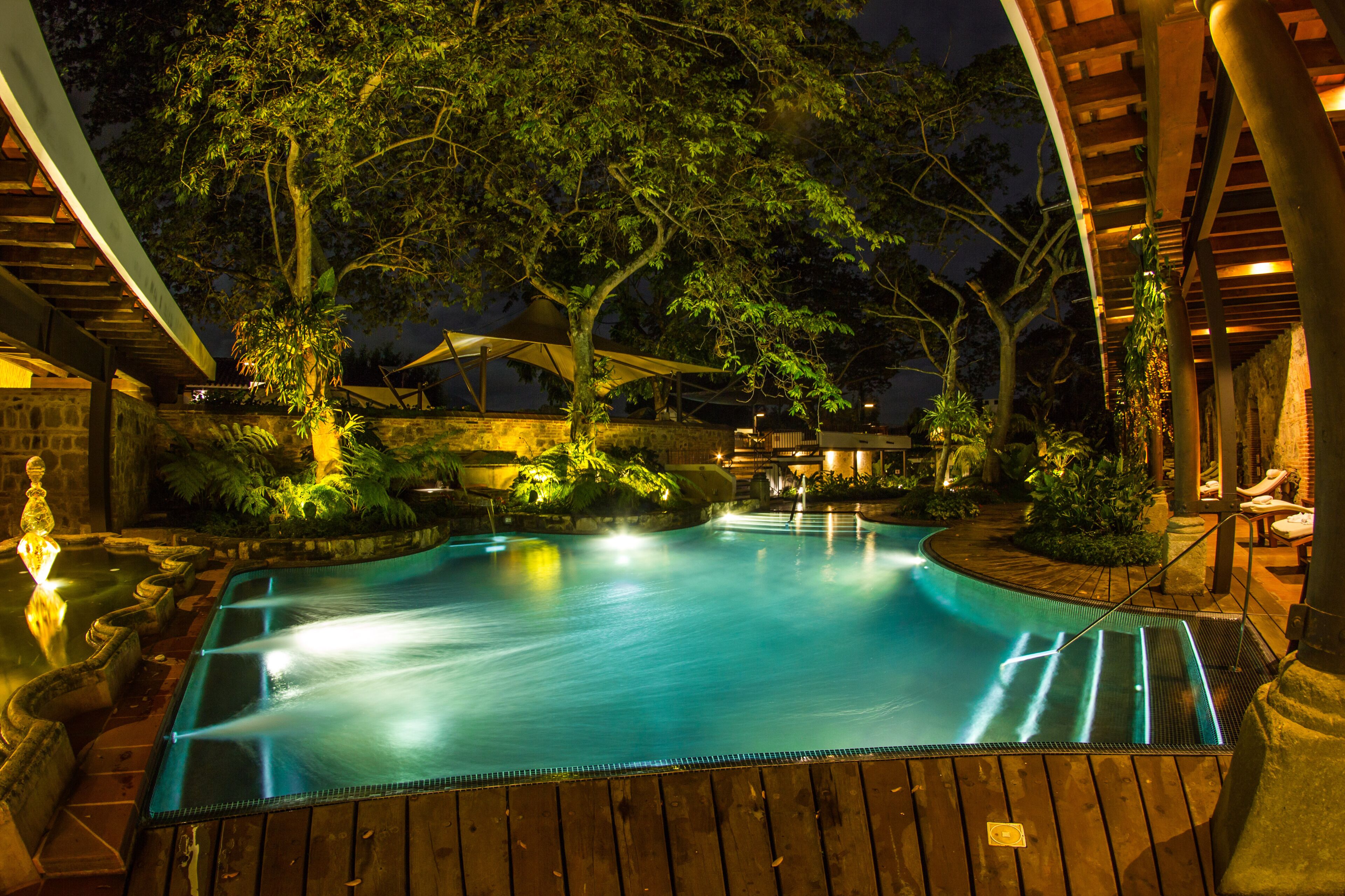 Una piscina con cubierta de madera, rodeada de árboles y un área techada con asientos.